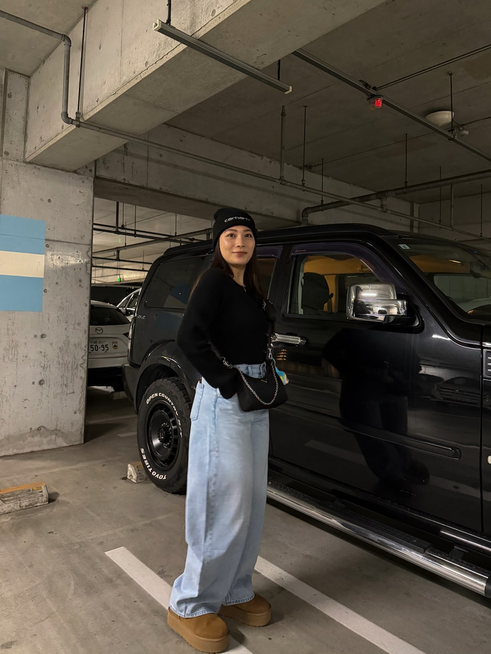 ベージュ系のブーツ、ブラック系のカーディガン/ボレロ、ブルー系のデニムパンツを着用したレディースの春コーディネートの2枚目の写真