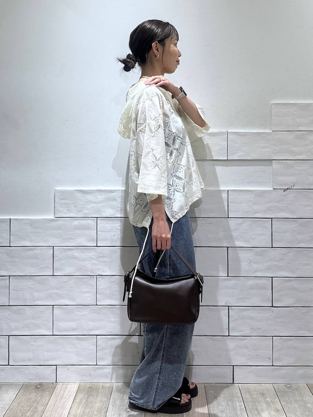 ブルー系のデニムパンツ、ブラウン系のショルダーバッグ、ホワイト系のシャツ/ブラウスを着用したレディースの夏コーディネートの2枚目の写真