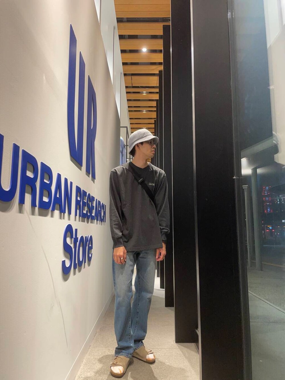 ベージュ系のサンダル、ブルー系のデニムパンツ、ブラック系のショルダーバッグを着用したメンズの秋コーディネートの2枚目の写真