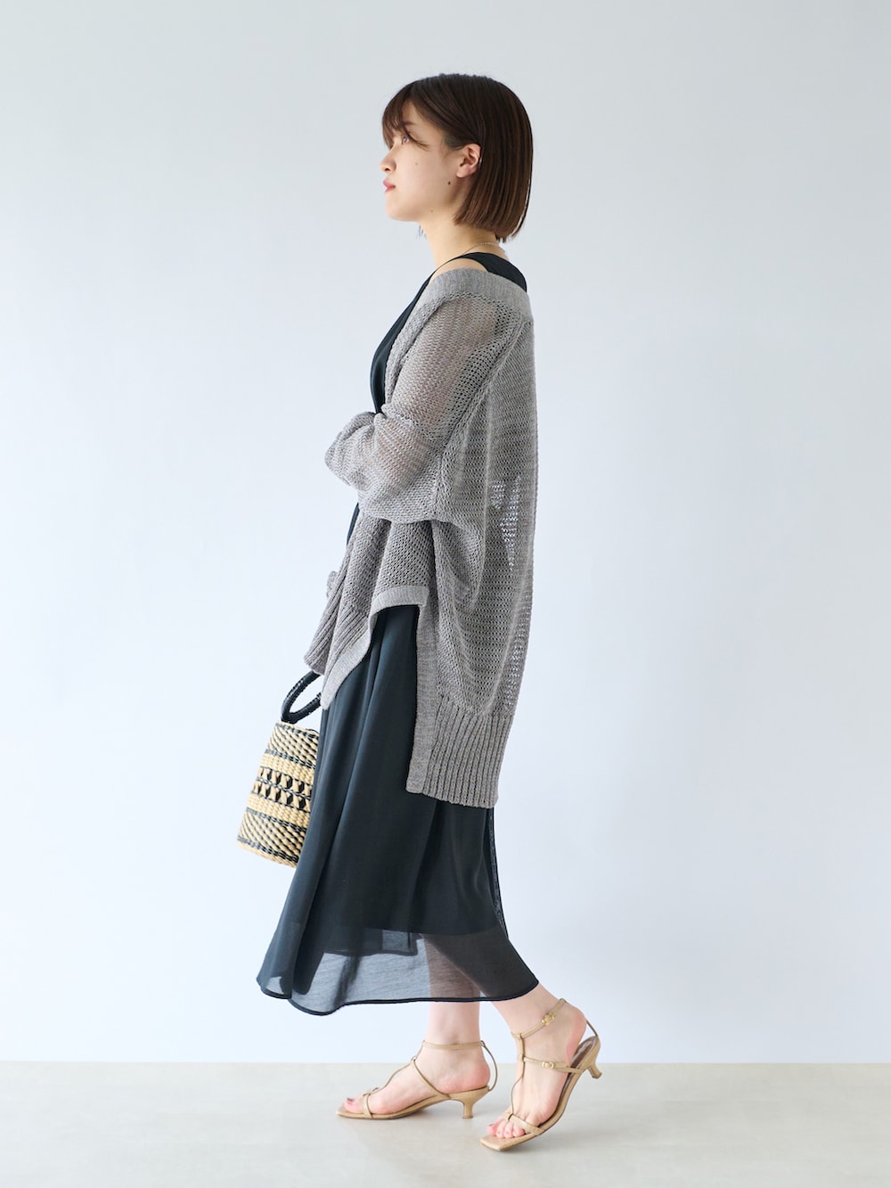 ブラック系のワンピース、グレー系のカーディガン/ボレロ、ベージュ系のかごバッグを着用したレディースの春コーディネートの2枚目の写真