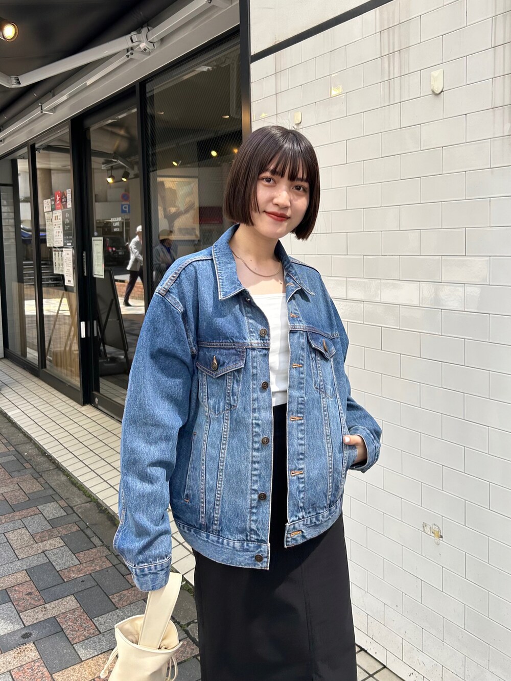 ブルー系のデニムジャケット、ブラック系のスカート、ホワイト系のハンドバッグを着用したレディースの春コーディネートの3枚目の写真