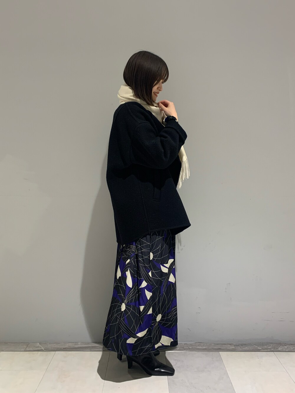 ブラック系のノーカラーコート、ブルー系のワンピース、ブラック系のブーツを着用したレディースの冬コーディネートの2枚目の写真