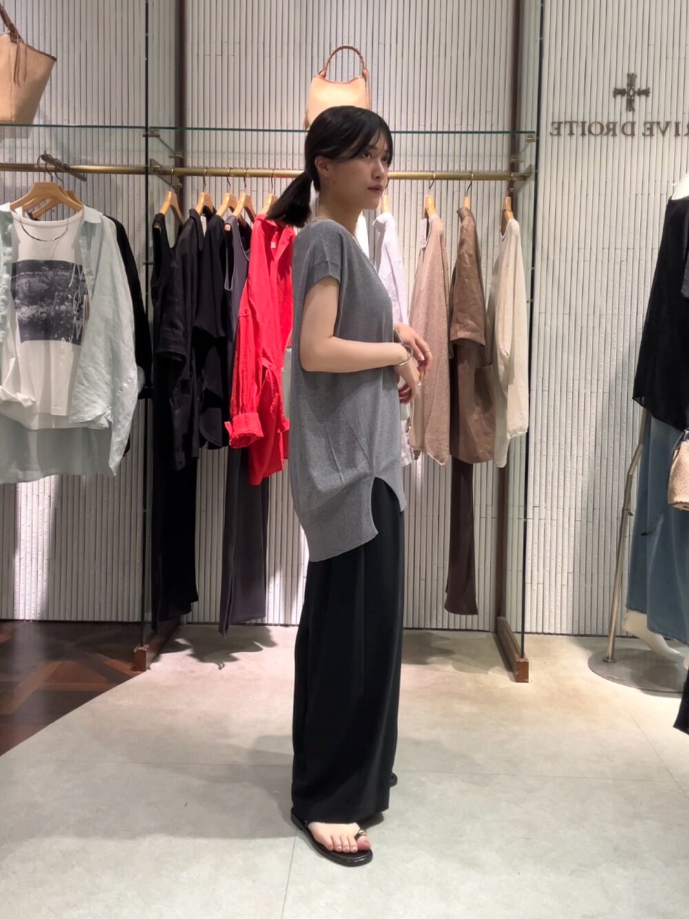 グレー系のニット/セーター、ブラック系のスラックス、ホワイト系のボディバッグ/ウエストポーチを着用したレディースの夏コーディネートの2枚目の写真