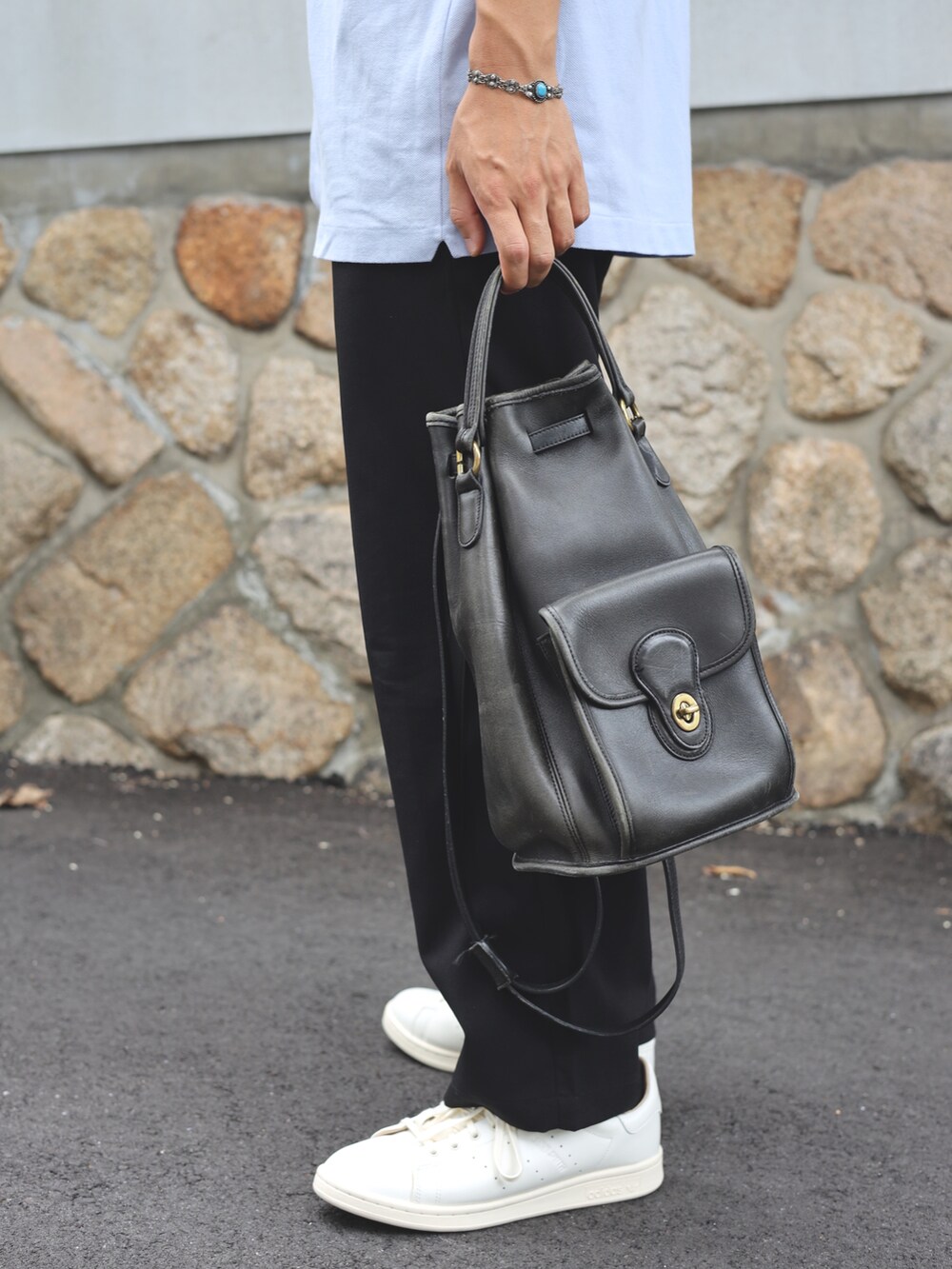 ブルー系のポロシャツ、ブラック系のショルダーバッグ、ホワイト系のスニーカーを着用したメンズの夏コーディネートの3枚目の写真