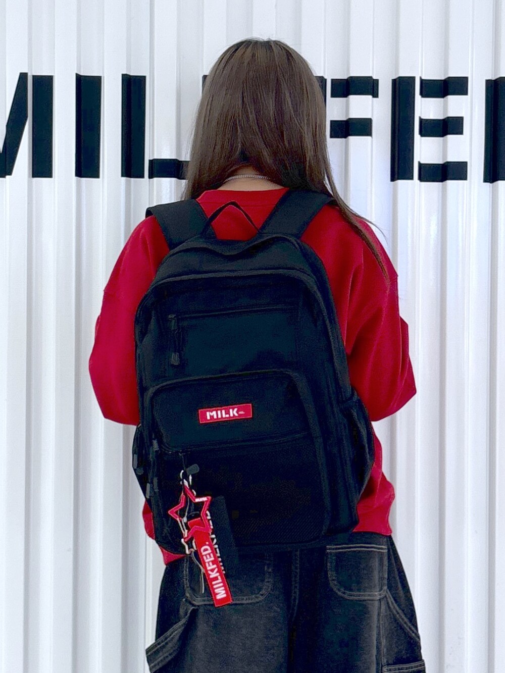 レッド系のスウェット、ホワイト系のデニムパンツ、レッド系のバックパック/リュックを着用したレディースの秋コーディネートの3枚目の写真