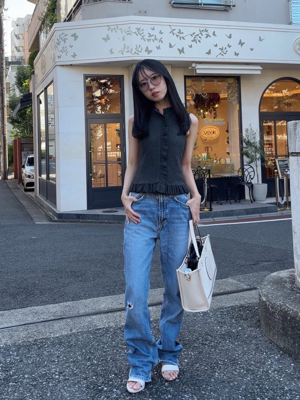 グレー系のトップス、ブルー系のデニムパンツ、ホワイト系のバッグを着用したレディースの夏コーディネートの2枚目の写真