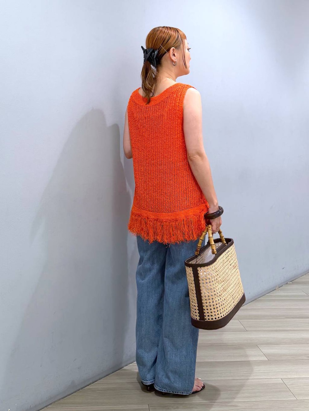 ブルー系のデニムパンツ、ベージュ系のかごバッグ、オレンジ系のニット/セーターを着用したレディースの夏コーディネートの5枚目の写真
