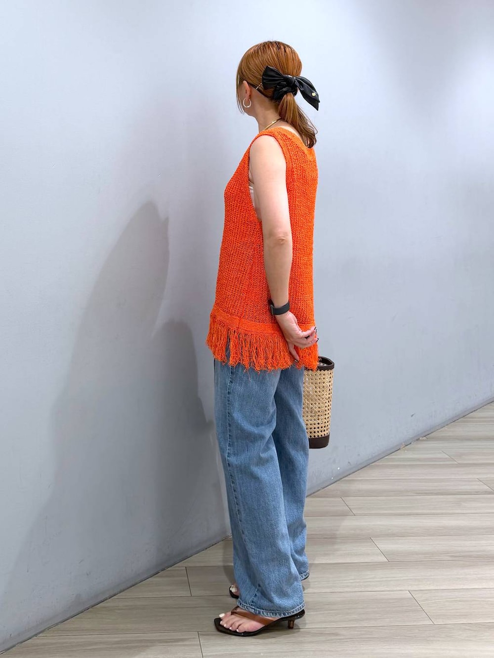 ブルー系のデニムパンツ、ベージュ系のかごバッグ、オレンジ系のニット/セーターを着用したレディースの夏コーディネートの4枚目の写真