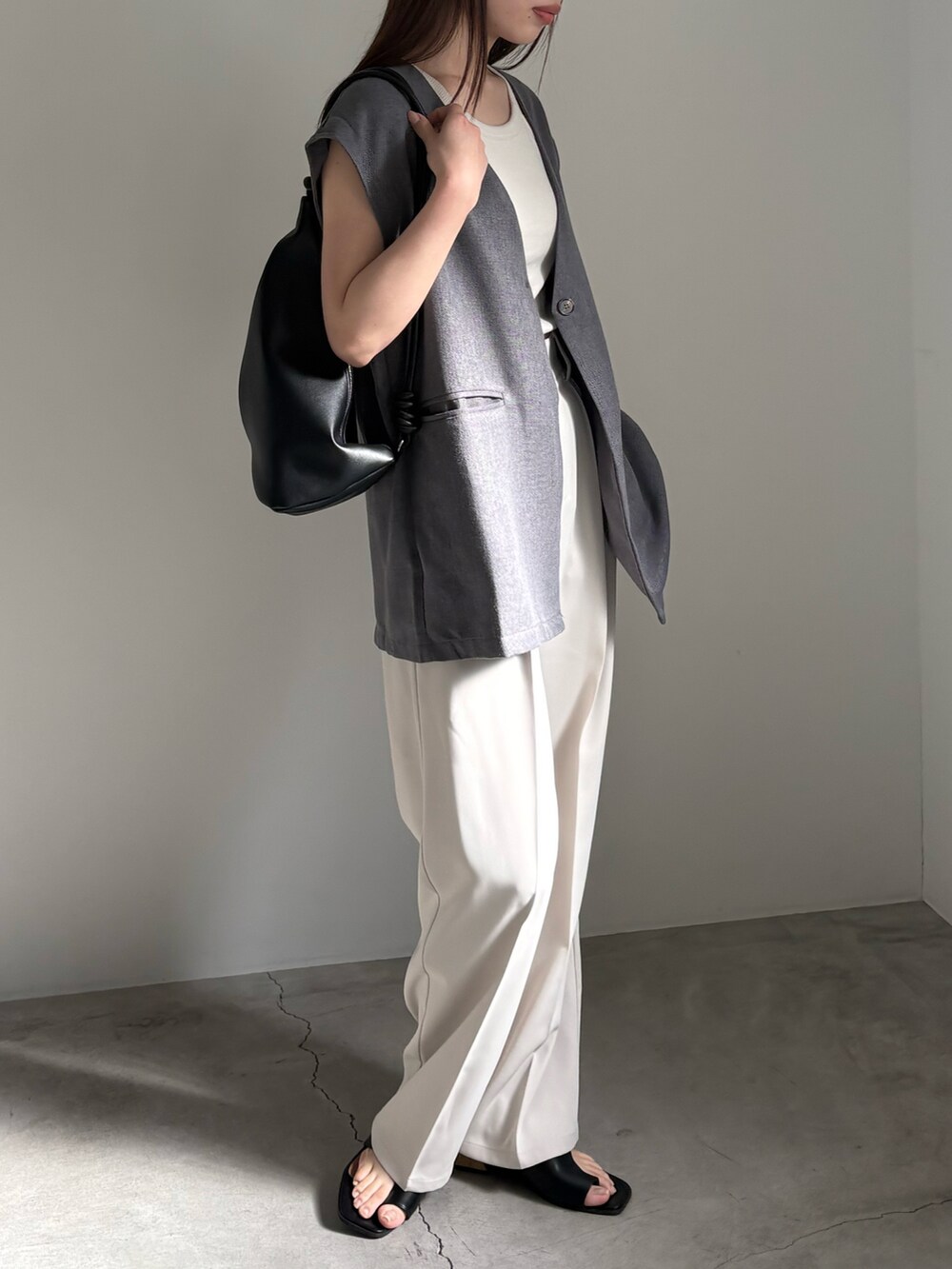 グレー系のベスト、ホワイト系のタンクトップ、ホワイト系のスラックスを着用したレディースの春コーディネートの2枚目の写真