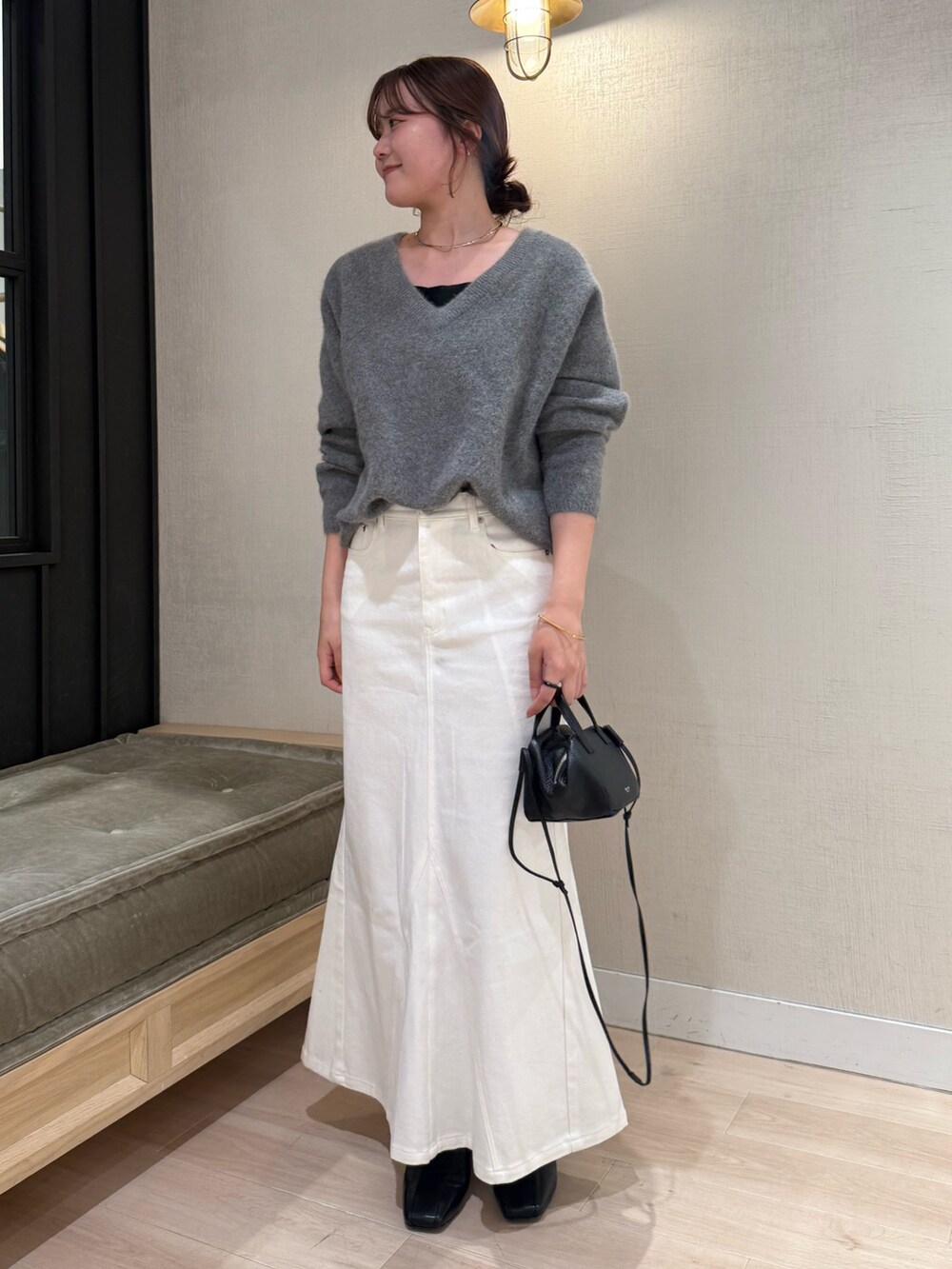 グレー系のニット/セーター、ホワイト系のデニムスカート、ブラック系のバッグを着用したレディースの秋コーディネートの2枚目の写真