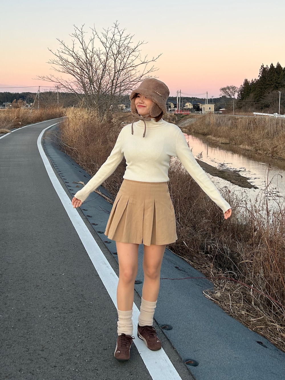 ベージュ系のスカート、ホワイト系のニット/セーター、ブラウン系のスニーカーを着用したレディースの冬コーディネートの2枚目の写真