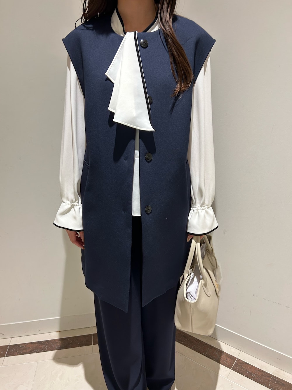 ブルー系のベスト、ホワイト系のシャツ/ブラウス、ベージュ系のトートバッグを着用したレディースの冬コーディネートの3枚目の写真