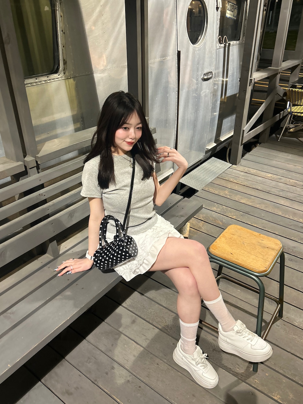 ブラック系のショルダーバッグ、ホワイト系のスカート、ホワイト系のスニーカーを着用したレディースの春コーディネートの2枚目の写真