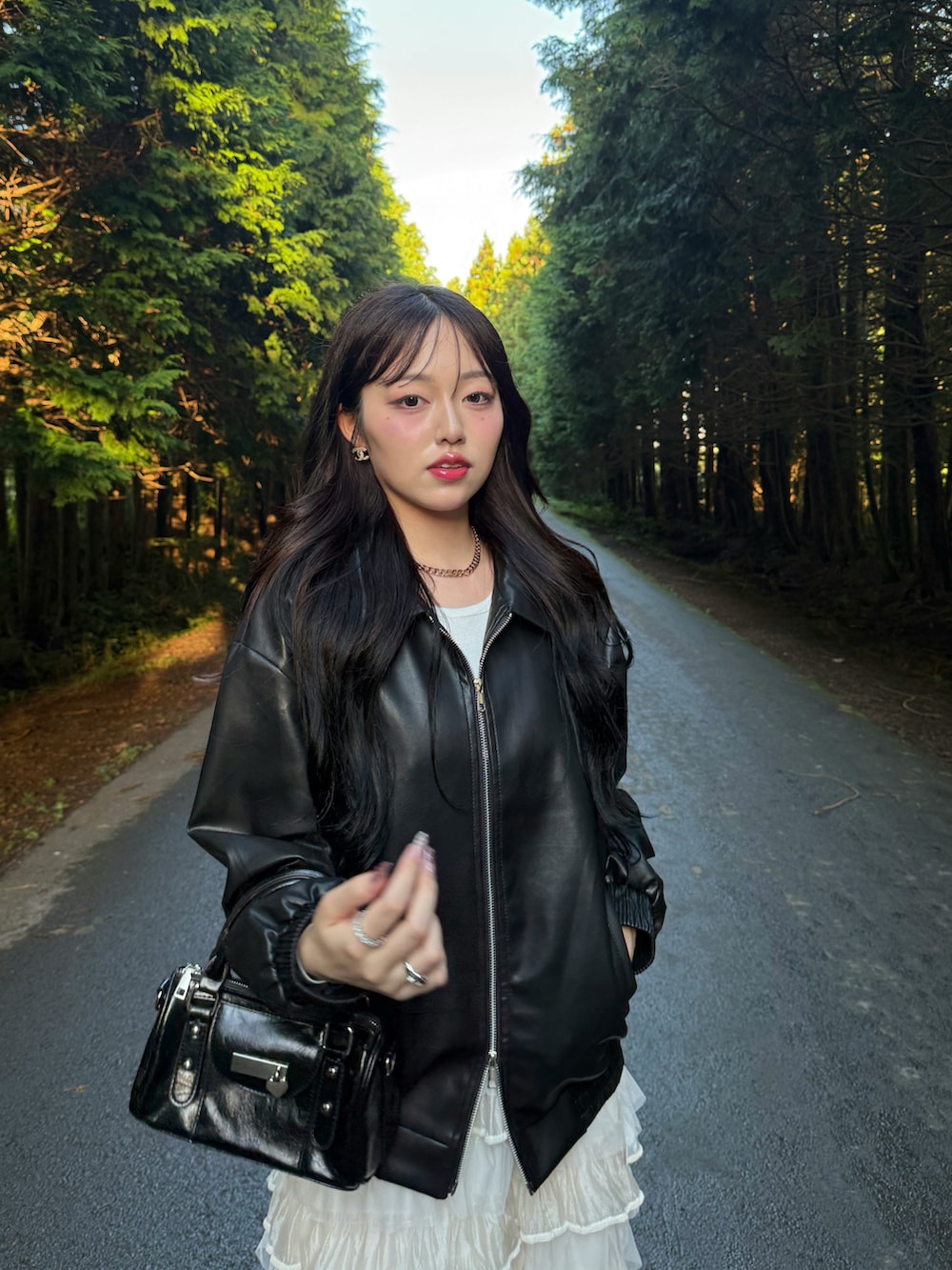 ブラック系のライダースジャケット、ホワイト系のスカート、ブラック系のスニーカーを着用したレディースの秋コーディネートの2枚目の写真