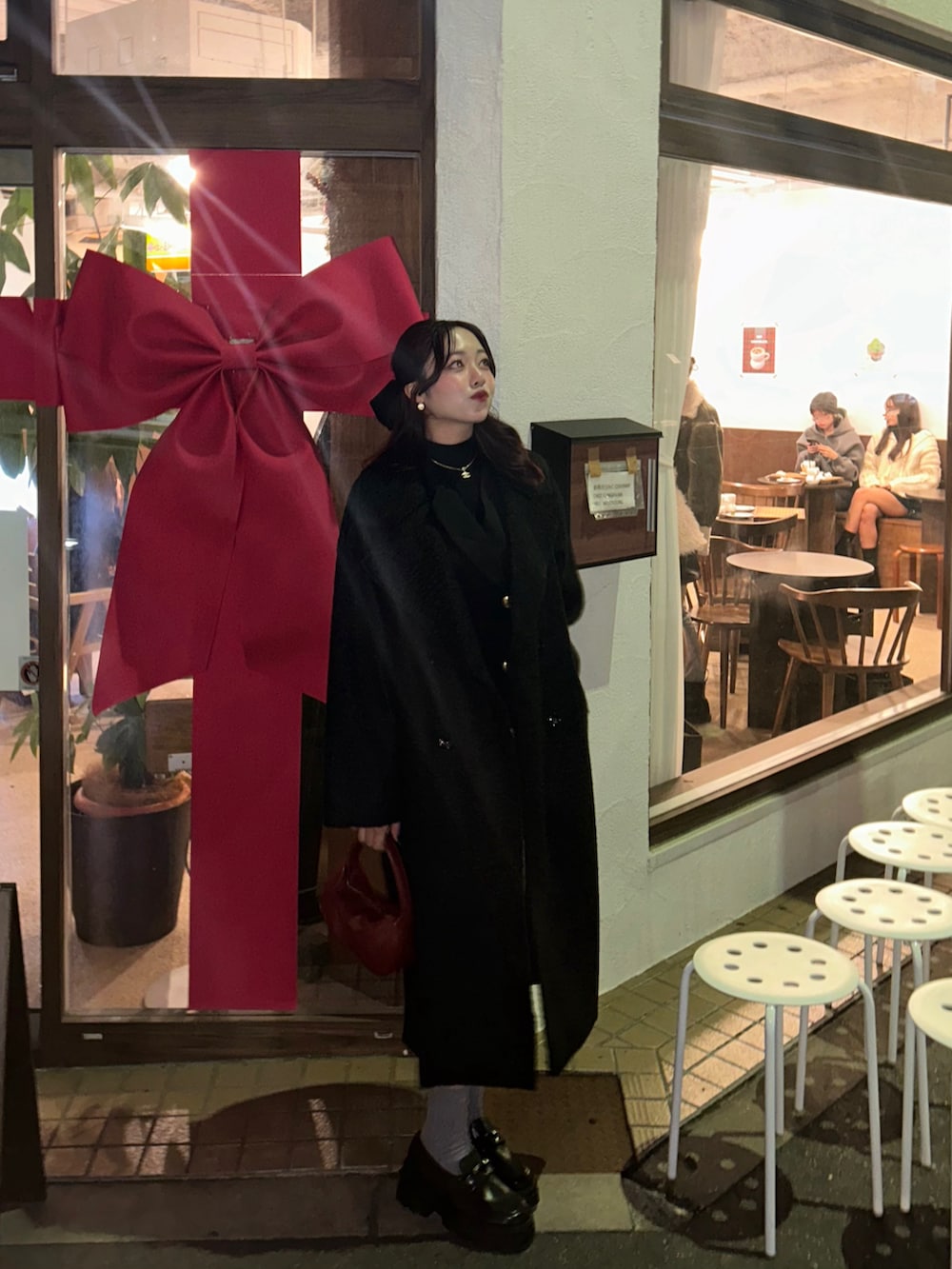 ブラック系のノーカラーコート、ブラック系のワンピース、レッド系のハンドバッグを着用したレディースの冬コーディネートの5枚目の写真