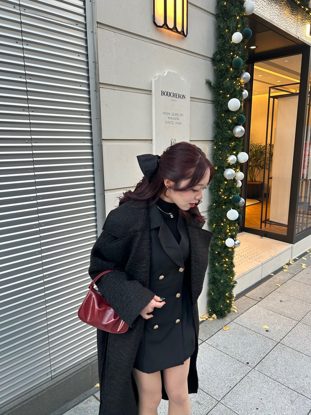 ブラック系のノーカラーコート、ブラック系のワンピース、レッド系のハンドバッグを着用したレディースの冬コーディネートの3枚目の写真