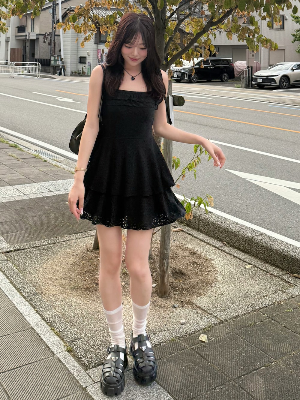 ブラック系のワンピース、ブラック系のサンダル、ブラウン系のハンドバッグを着用したレディースの夏コーディネートの2枚目の写真