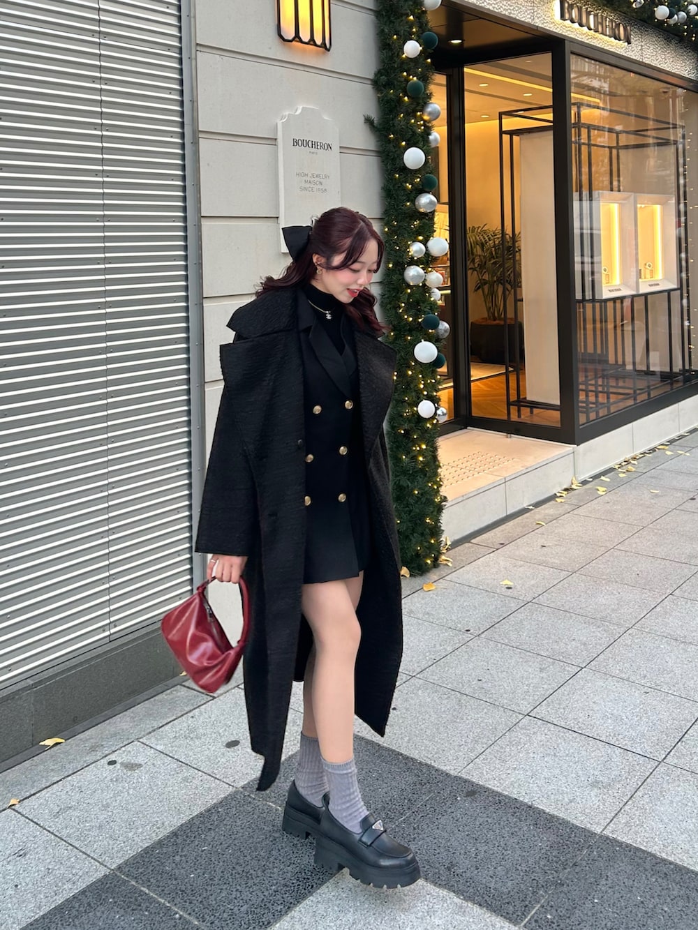 ブラック系のノーカラーコート、ブラック系のワンピース、レッド系のハンドバッグを着用したレディースの冬コーディネートの2枚目の写真