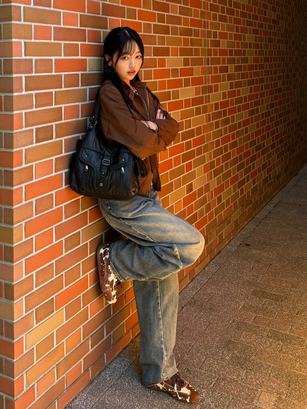 ブラウン系のスニーカー、ブラウン系のライダースジャケット、ブルー系のデニムパンツを着用したレディースの秋コーディネートの2枚目の写真