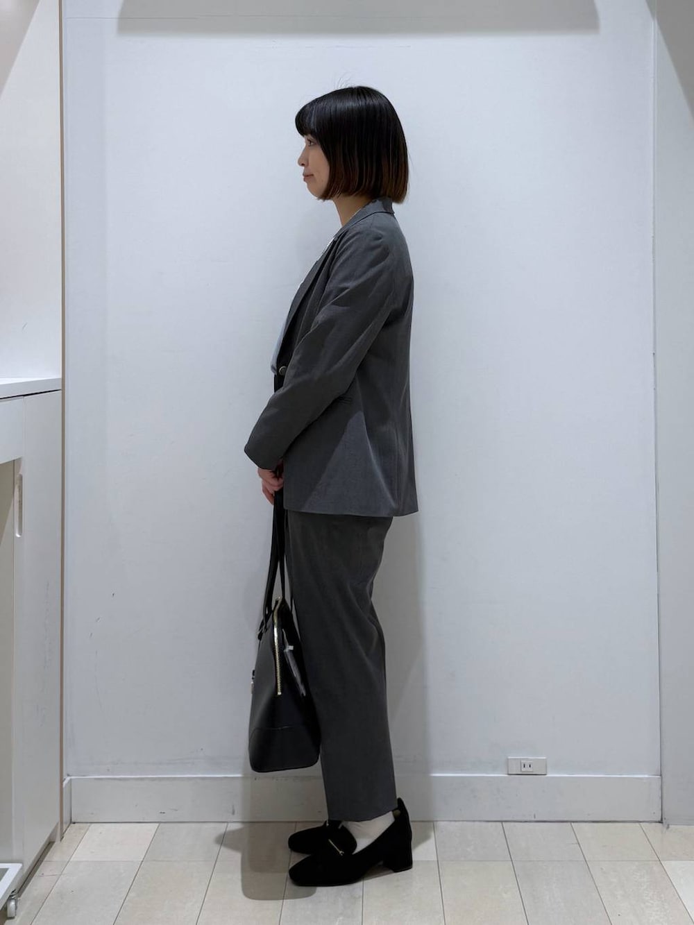 ブラック系のローファー、グレー系のスラックス、ブラック系のボストンバッグを着用したレディースの冬コーディネートの2枚目の写真