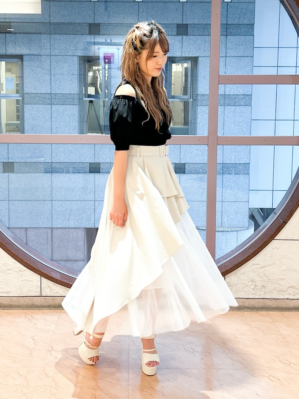 ベージュ系のスカート、ブラック系のニット/セーターを着用したレディースの夏コーディネートの2枚目の写真