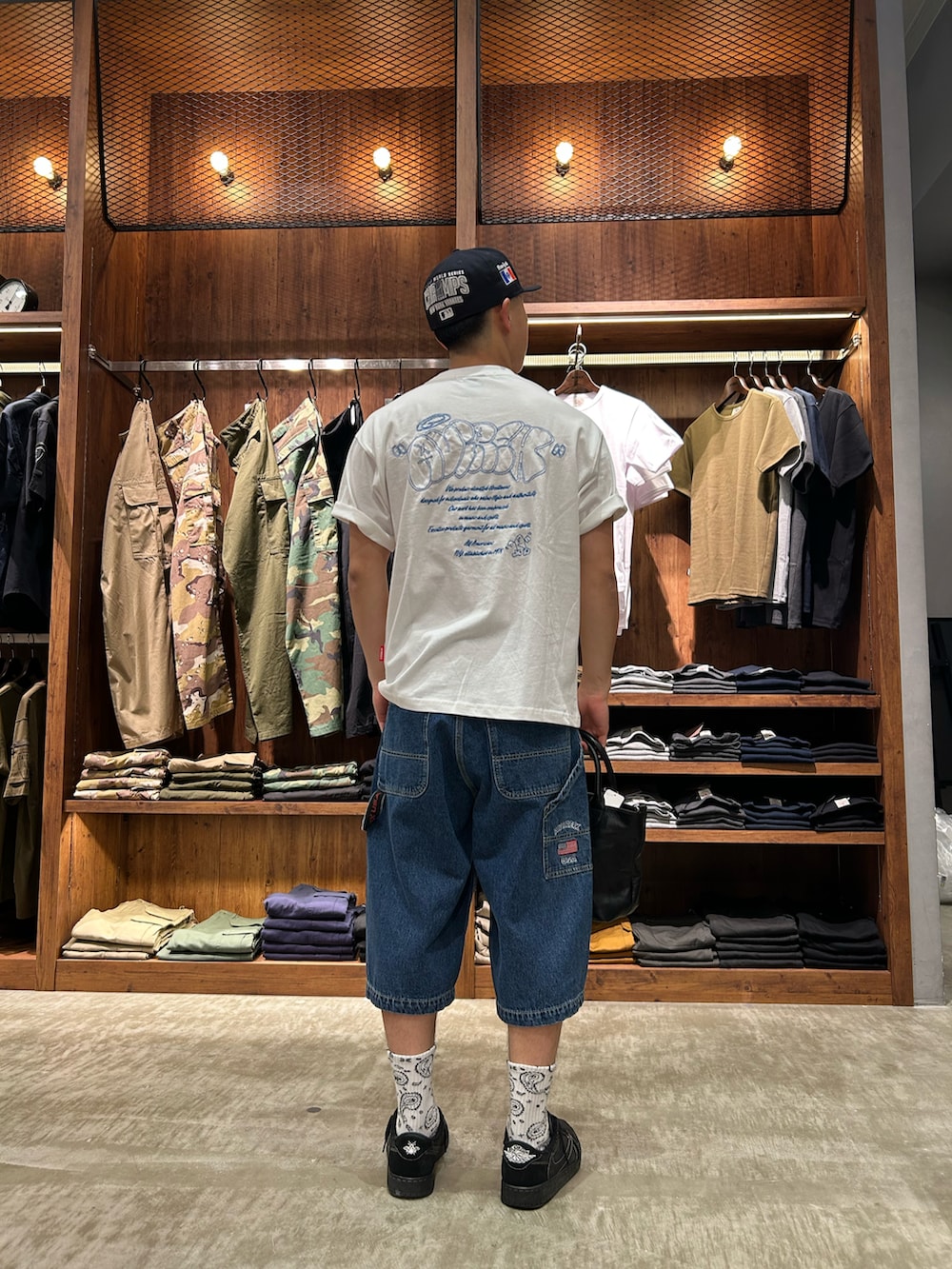 ブルー系のデニムパンツ、ブラック系のトートバッグ、ホワイト系のTシャツ/カットソーを着用したメンズの夏コーディネートの2枚目の写真