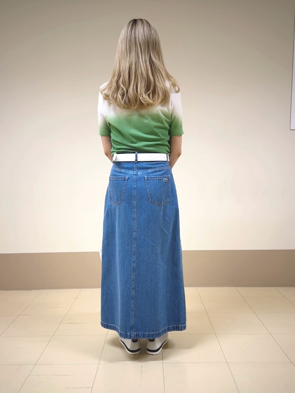 グリーン系のニット/セーター、ブルー系のデニムスカート、ホワイト系のスニーカーを着用したレディースの春コーディネートの2枚目の写真