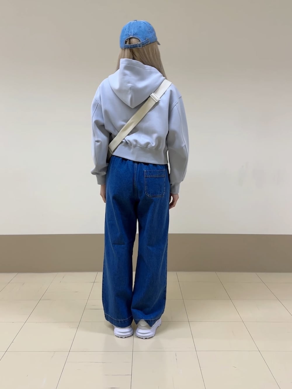 ブルー系のデニムパンツ、ホワイト系のスニーカー、ホワイト系のメッセンジャーバッグを着用したレディースの冬コーディネートの2枚目の写真