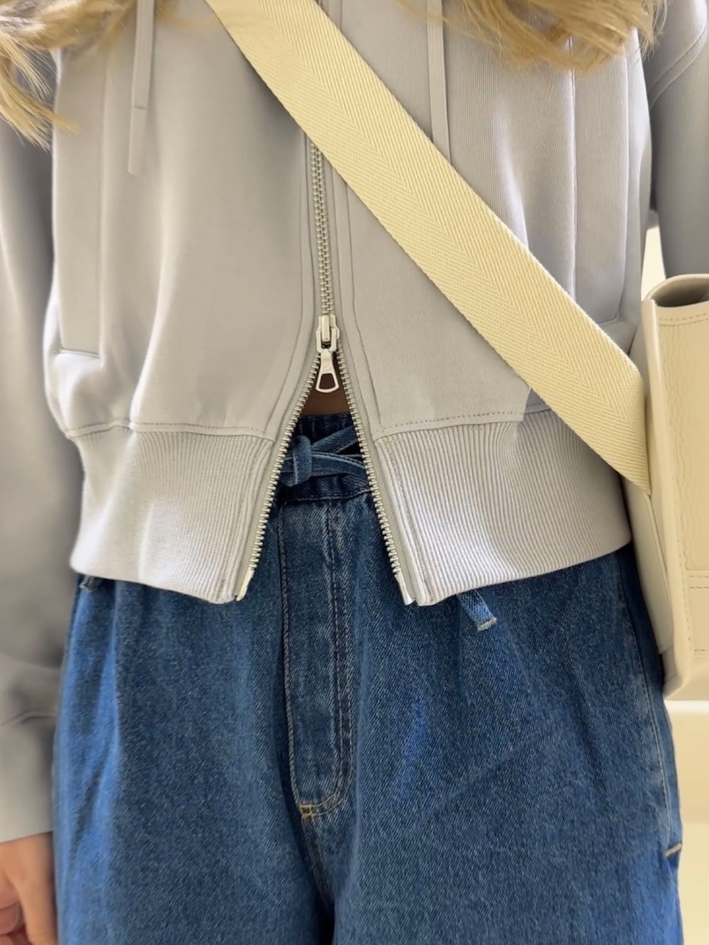 ブルー系のデニムパンツ、ホワイト系のスニーカー、ホワイト系のメッセンジャーバッグを着用したレディースの冬コーディネートの3枚目の写真