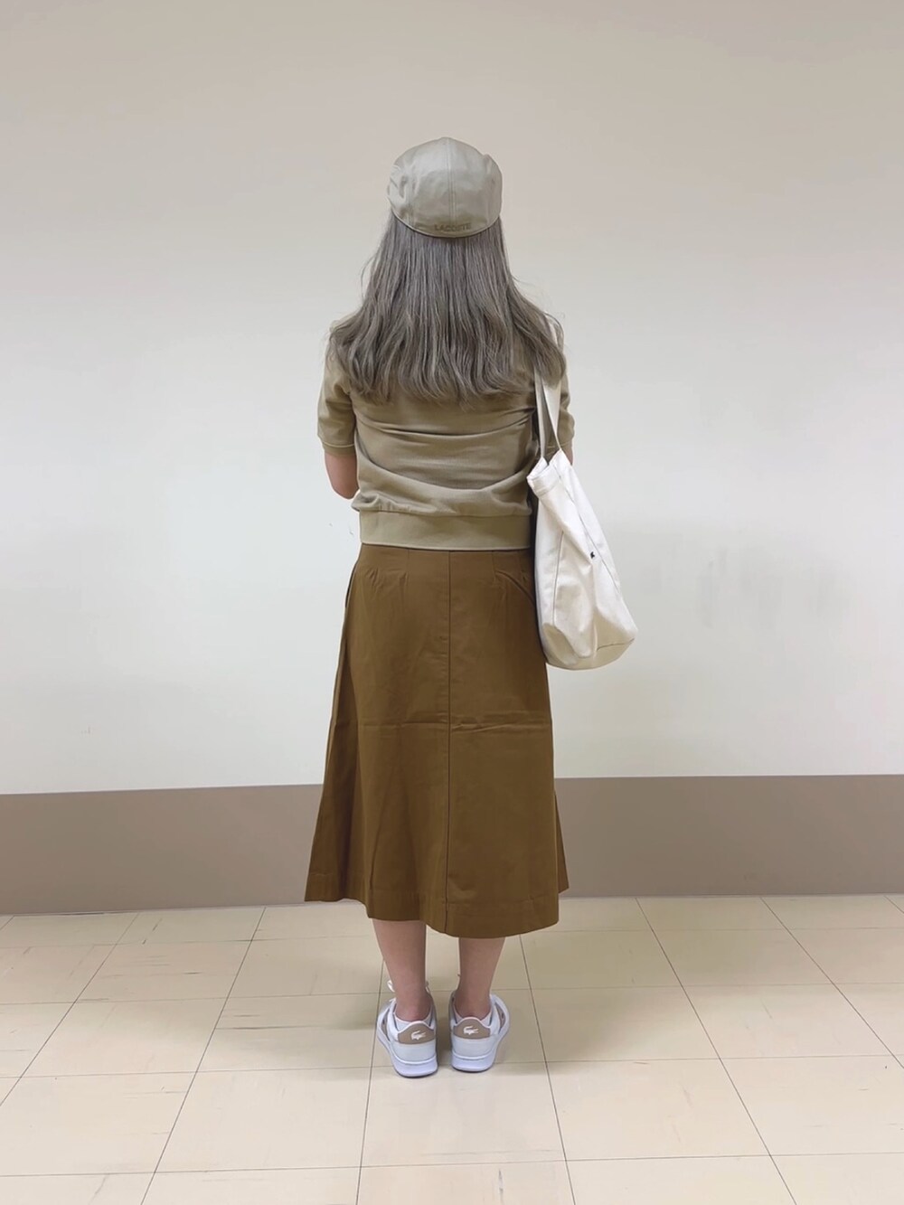 ブラウン系のスカート、ベージュ系のポロシャツ、ホワイト系のスニーカーを着用したレディースの夏コーディネートの2枚目の写真