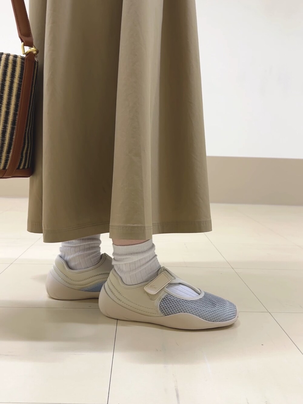 ベージュ系のワンピース、ベージュ系のハンドバッグ、ホワイト系のスニーカーを着用したレディースの春コーディネートの4枚目の写真