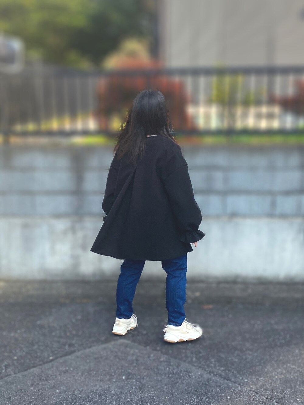 ブラック系のノーカラーコート、ブルー系のデニムパンツ、ベージュ系のスニーカーを着用したレディースの秋コーディネートの3枚目の写真