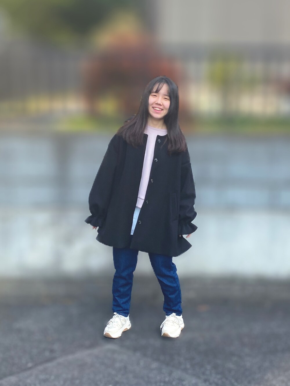 ブラック系のノーカラーコート、ブルー系のデニムパンツ、ベージュ系のスニーカーを着用したレディースの秋コーディネートの2枚目の写真