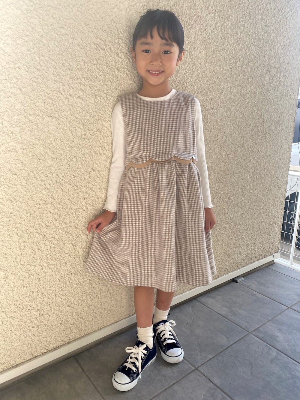 ベージュ系のワンピース、ホワイト系のTシャツ/カットソー、ブラック系のスニーカーを着用したキッズの秋コーディネートの2枚目の写真