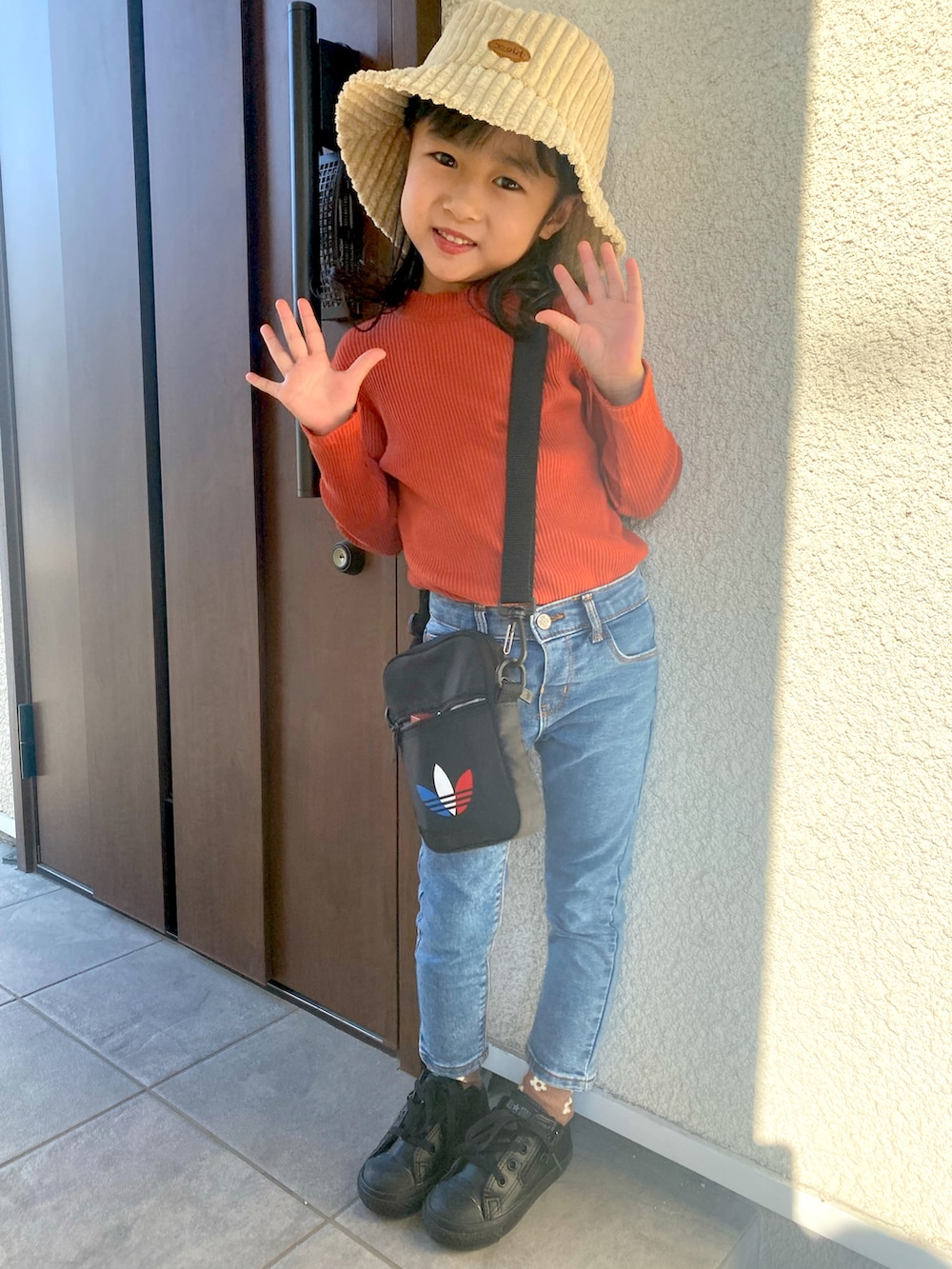 オレンジ系のトップス、ブルー系のデニムパンツ、ブラック系のスニーカーを着用したキッズの秋コーディネートの2枚目の写真