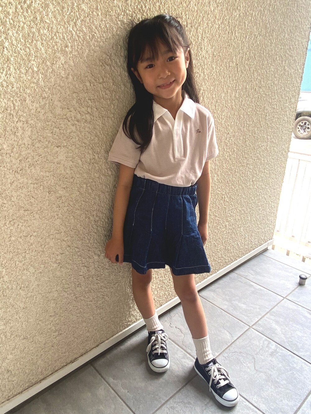 ベージュ系のポロシャツ、ブルー系のデニムスカート、ブラック系のスニーカーを着用したキッズの夏コーディネートの3枚目の写真