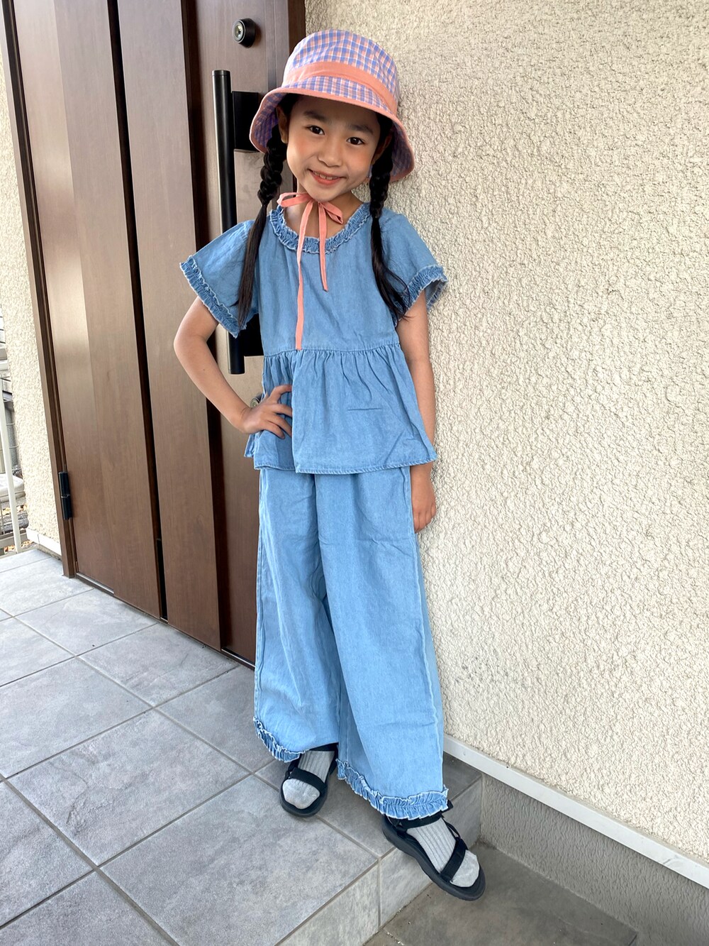 ブルー系のセットアップ、ブラック系のサンダル、ピンク系のハットを着用したキッズの春コーディネートの2枚目の写真