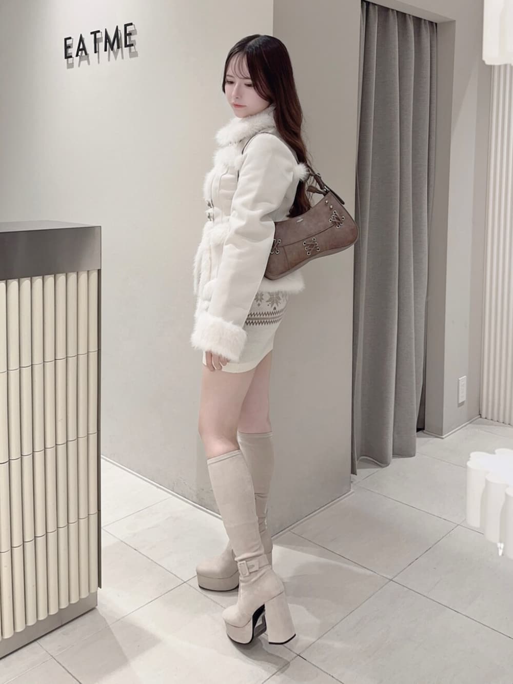 ブラウン系のショルダーバッグ、ホワイト系のブーツ、ホワイト系のスカートを着用したレディースの秋コーディネートの3枚目の写真