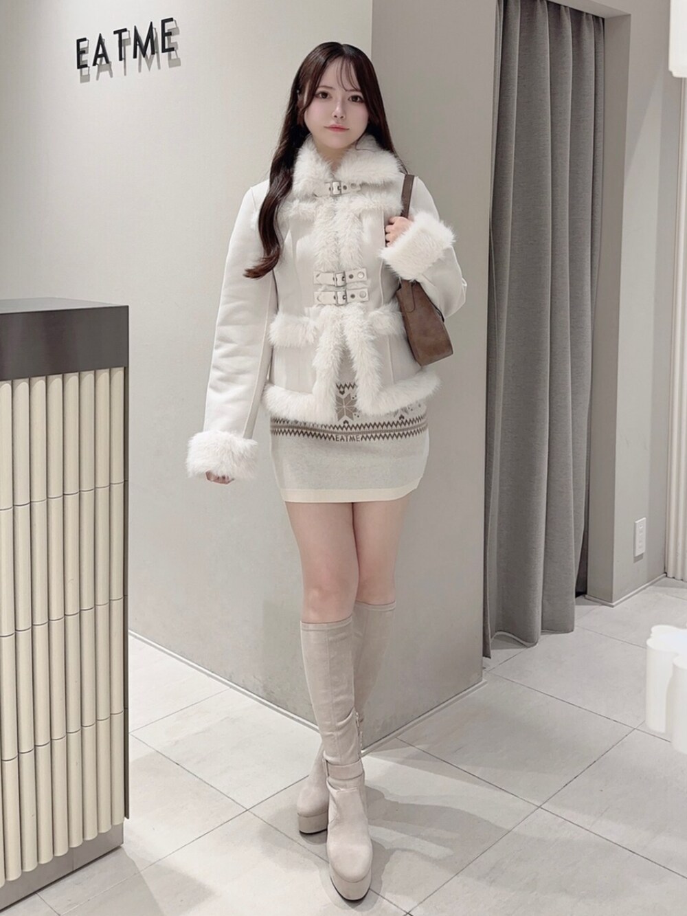 ブラウン系のショルダーバッグ、ホワイト系のブーツ、ホワイト系のスカートを着用したレディースの秋コーディネートの2枚目の写真