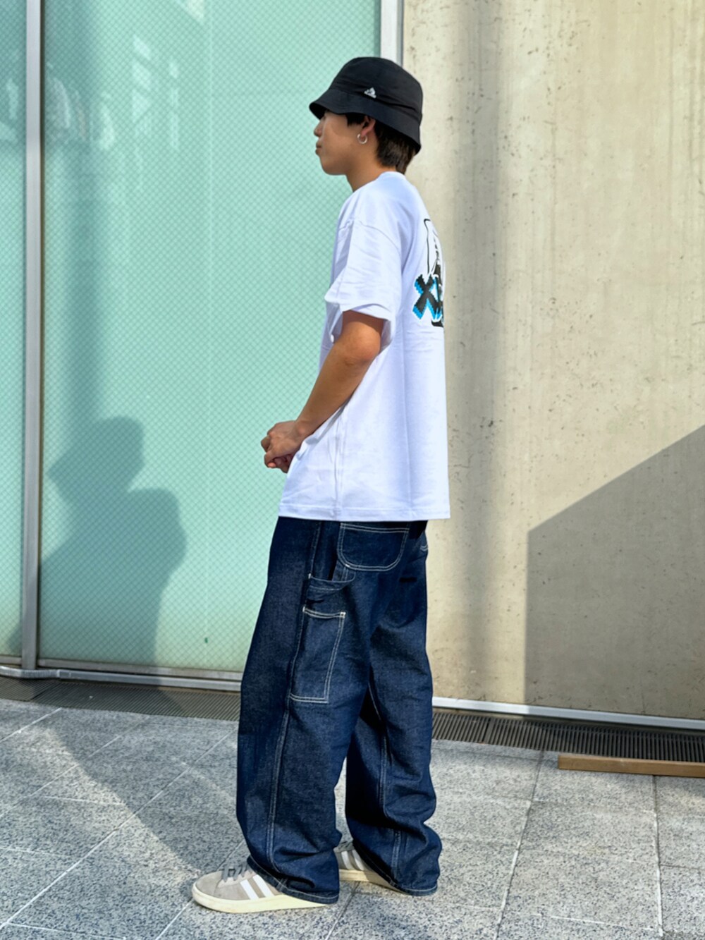 ホワイト系のTシャツ/カットソー、ブルー系のデニムパンツ、ブラック系のハットを着用したメンズの春コーディネートの2枚目の写真