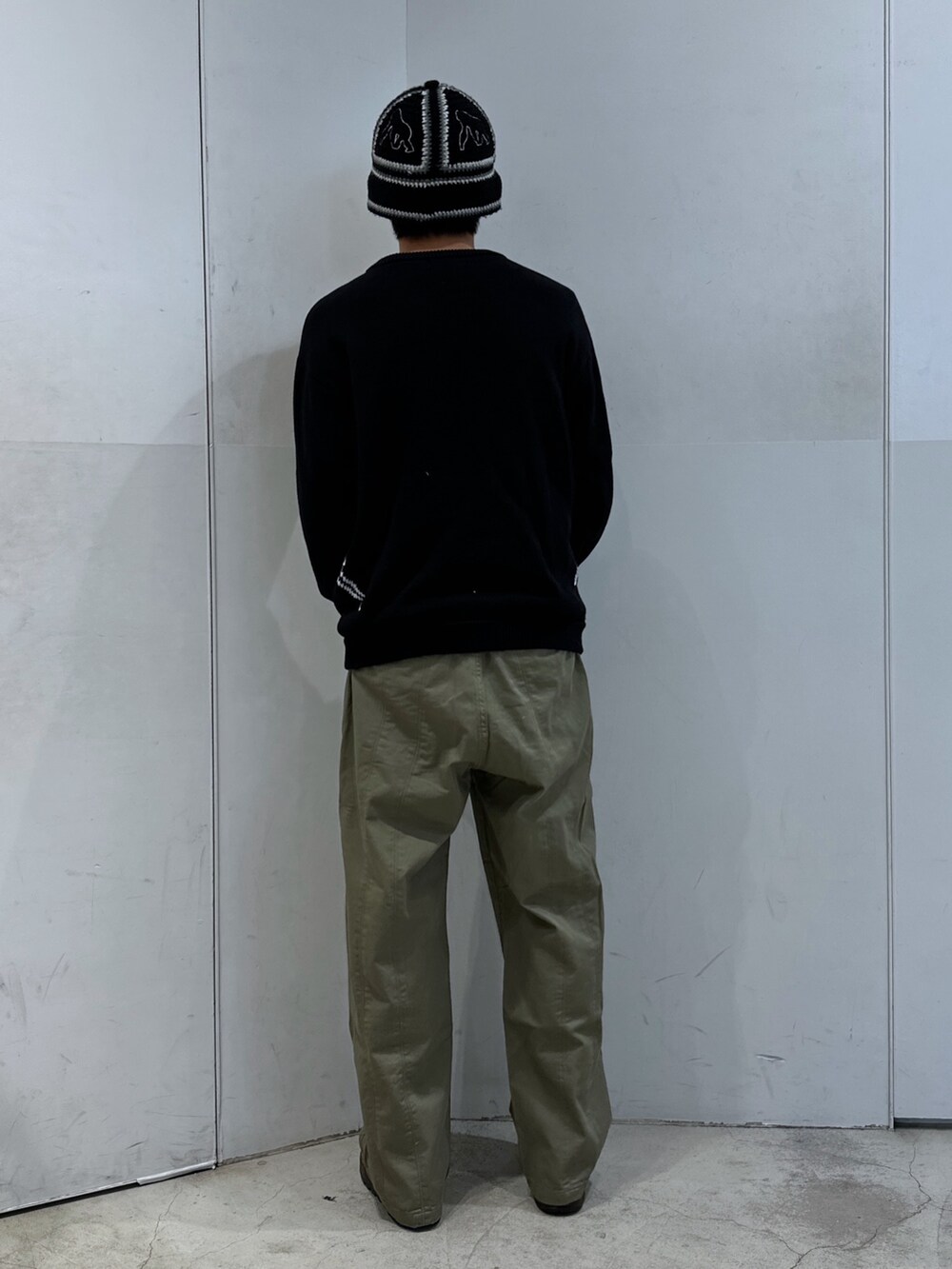 ブラック系のニット/セーター、グリーン系のチノパンツ、ブラック系のハットを着用したメンズの春コーディネートの3枚目の写真