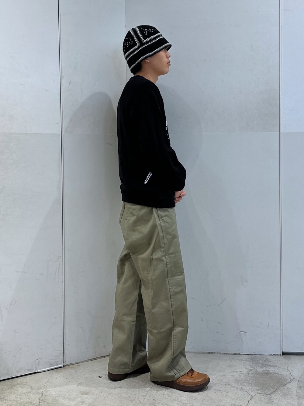 ブラック系のニット/セーター、グリーン系のチノパンツ、ブラック系のハットを着用したメンズの春コーディネートの4枚目の写真