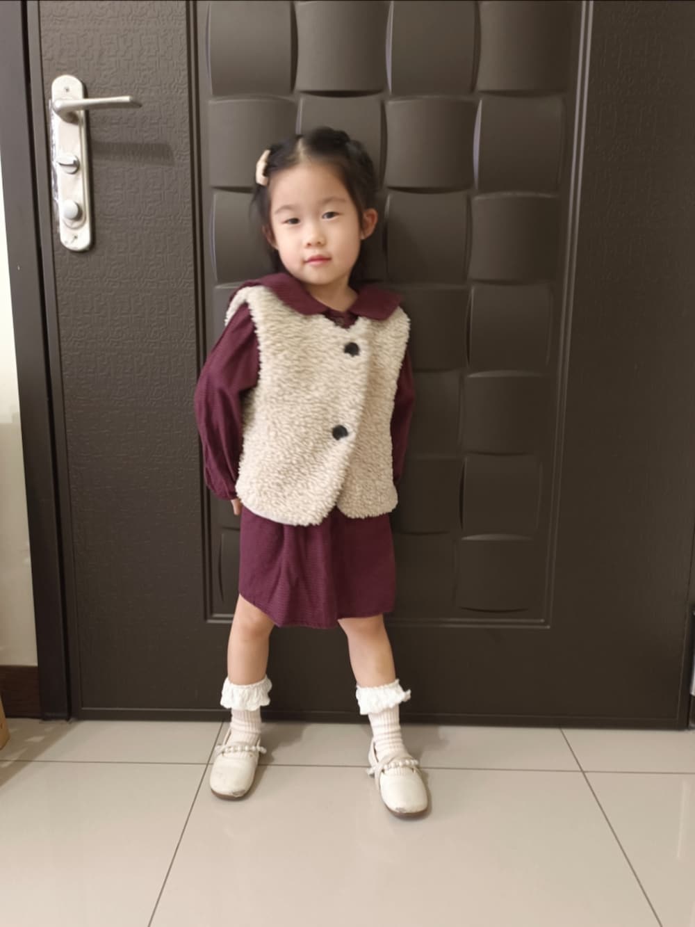 ベージュ系のその他アウター、ブラウン系のワンピース、ホワイト系のバレエシューズを着用したキッズの冬コーディネートの2枚目の写真