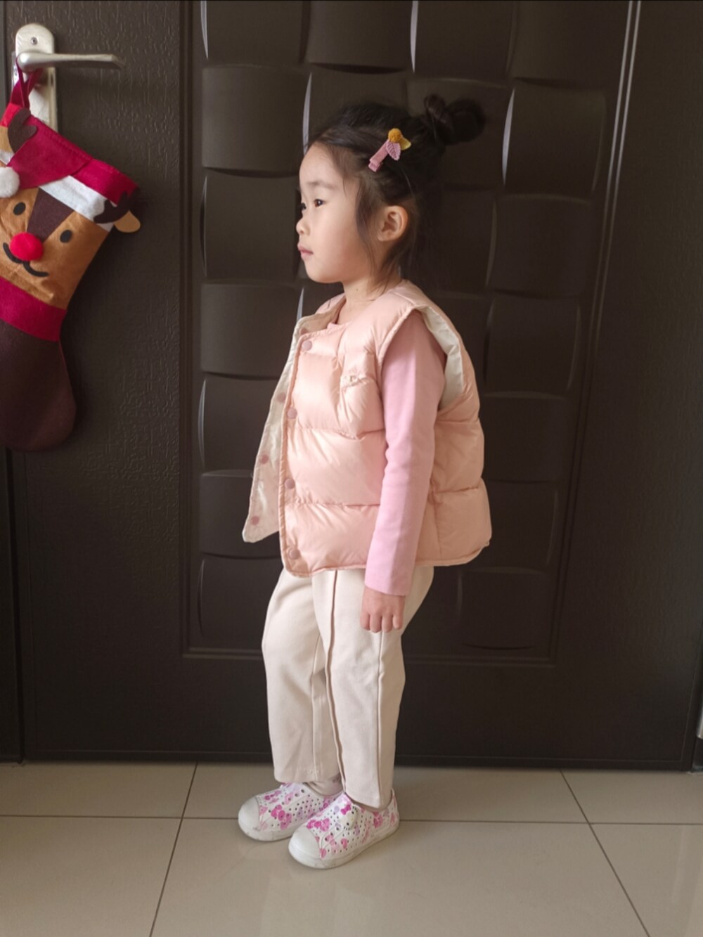ピンク系のTシャツ/カットソー、ピンク系のダウンベスト、ベージュ系のチノパンツを着用したキッズの冬コーディネートの2枚目の写真