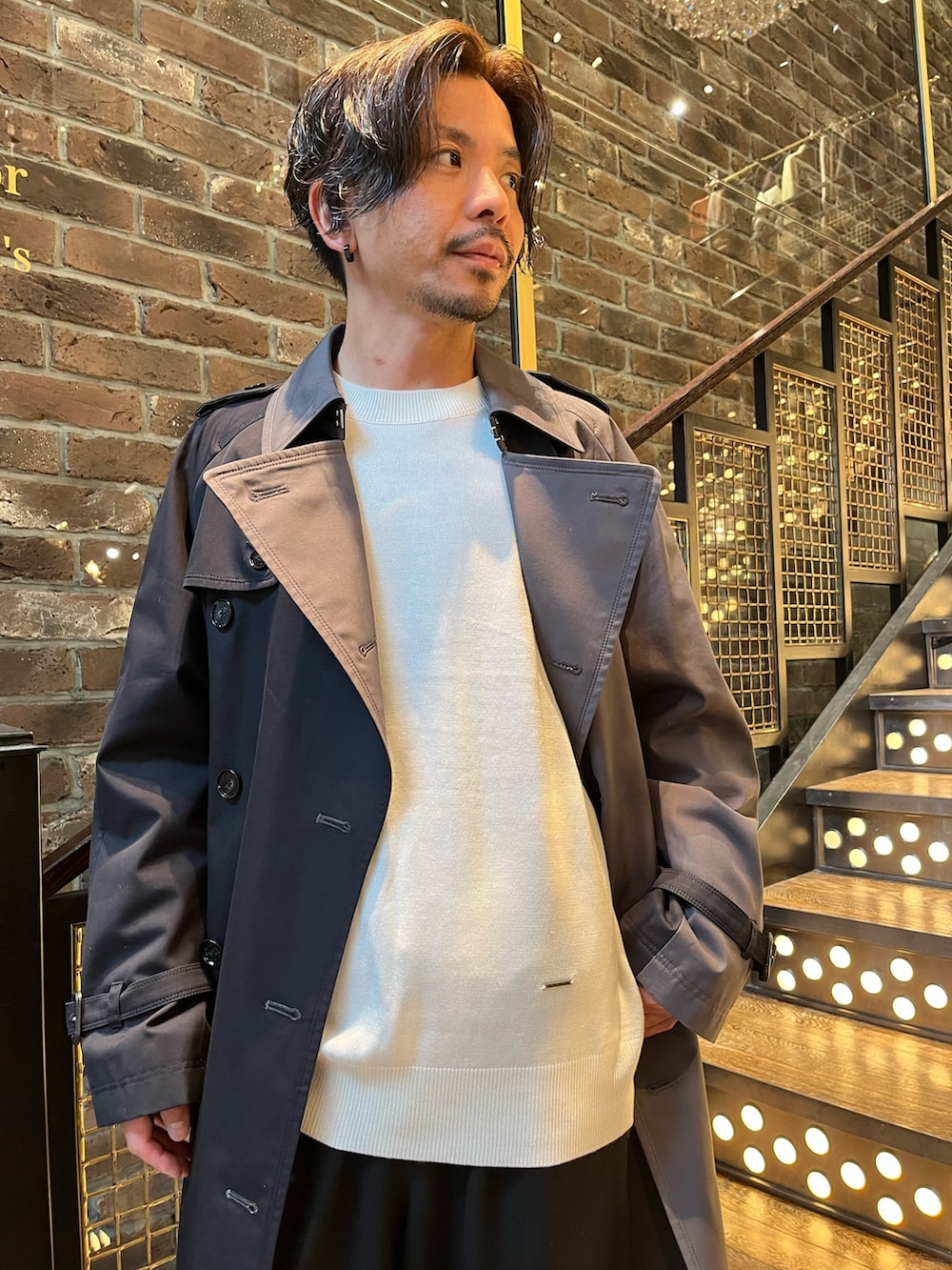 グレー系のトレンチコート、ホワイト系のニット/セーター、ブラック系のその他パンツを着用したメンズの秋コーディネートの2枚目の写真