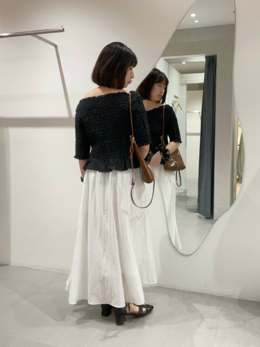 ブラウン系のショルダーバッグ、ホワイト系のスカート、ブラック系のシャツ/ブラウスを着用したレディースの春コーディネートの2枚目の写真