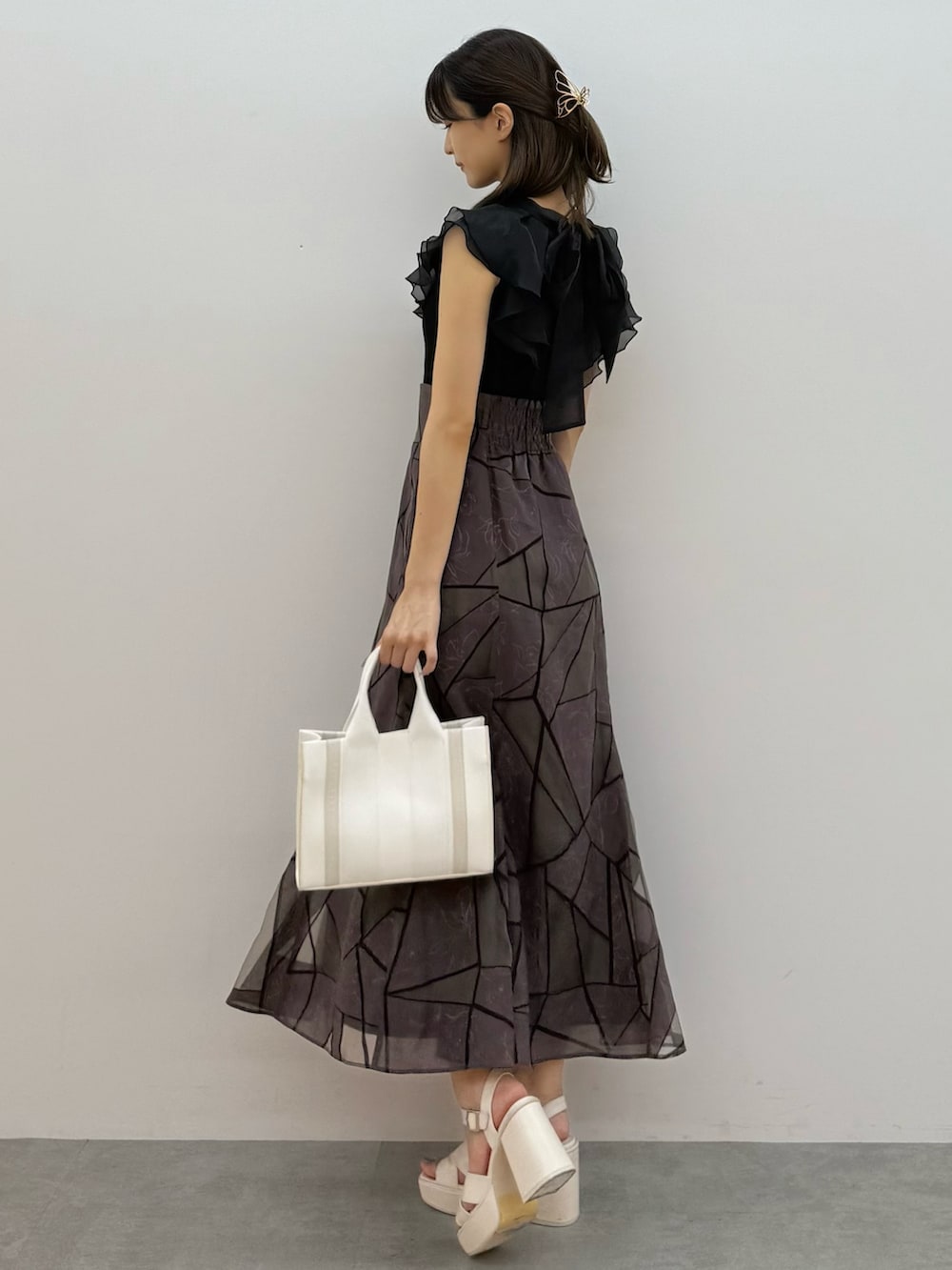 ブラック系のニット/セーター、ブラウン系のスカート、ホワイト系のトートバッグを着用したレディースの夏コーディネートの3枚目の写真