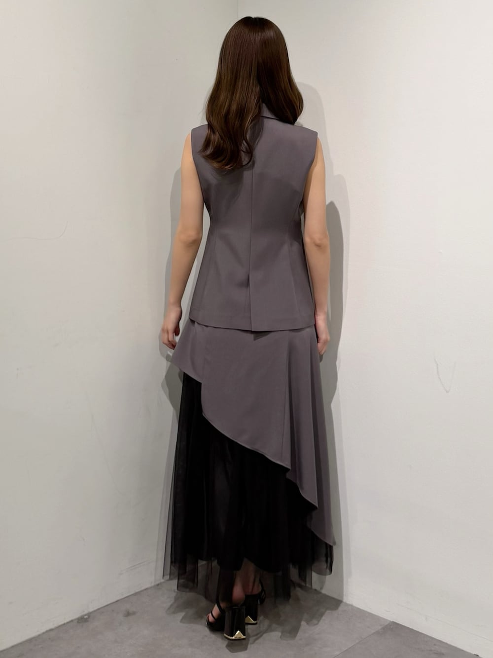 グレー系のベスト、グレー系のスカート、ブラック系のサンダルを着用したレディースの春コーディネートの5枚目の写真