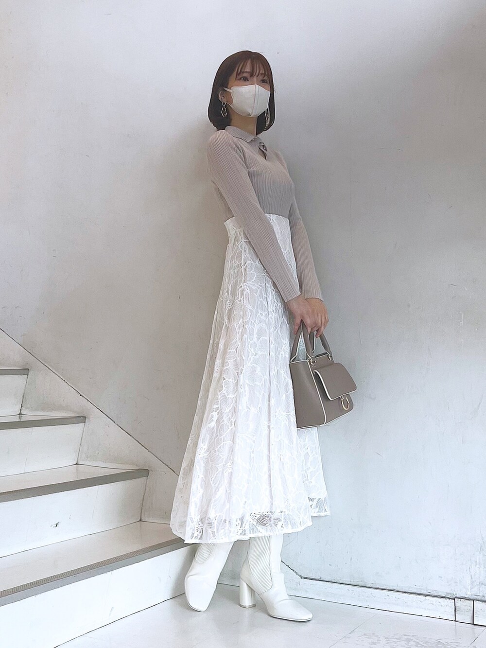 ベージュ系のハンドバッグ、ホワイト系のブーツ、ホワイト系のスカートを着用したレディースの冬コーディネートの2枚目の写真