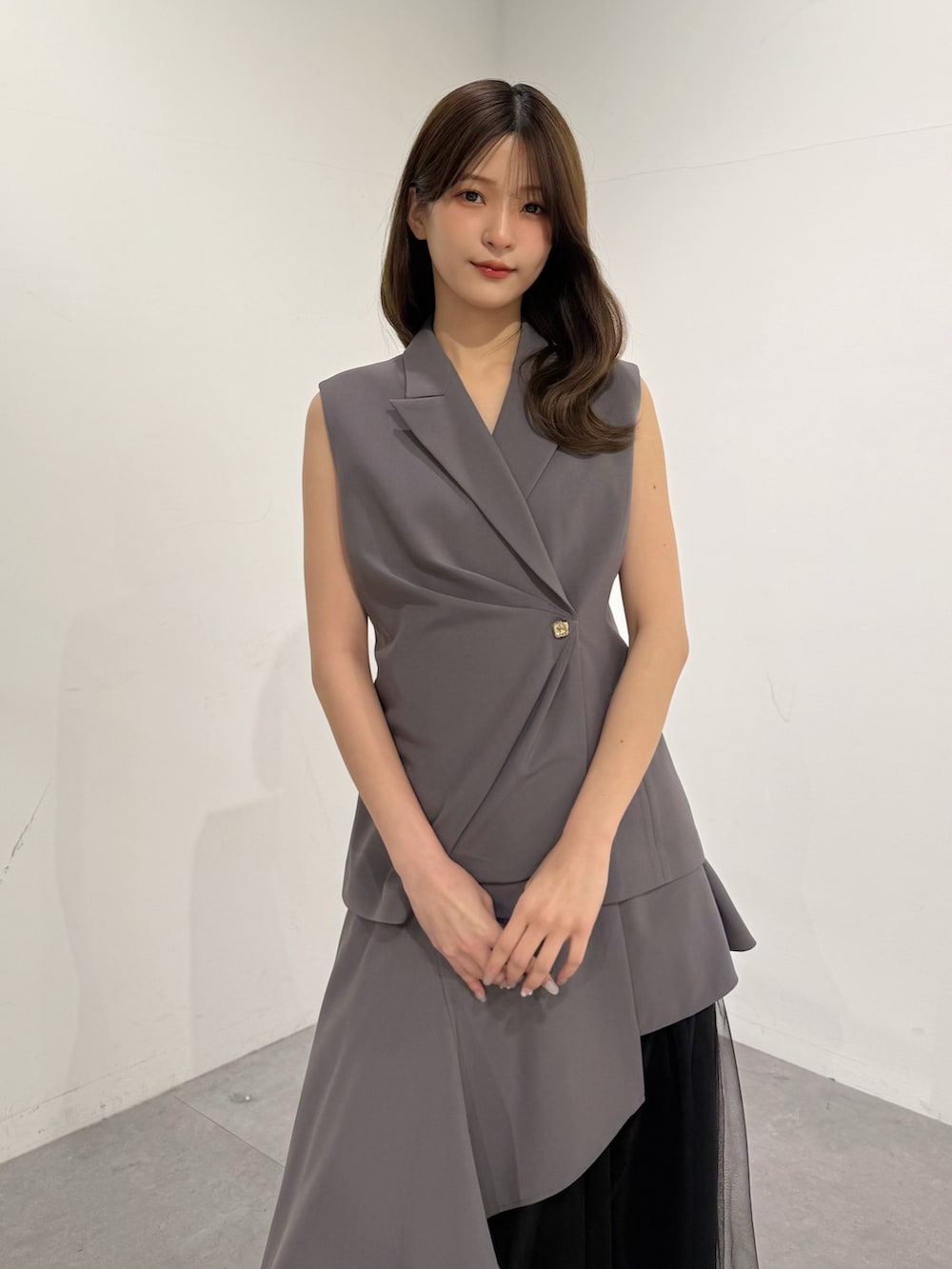 グレー系のベスト、グレー系のスカート、ブラック系のサンダルを着用したレディースの春コーディネートの2枚目の写真